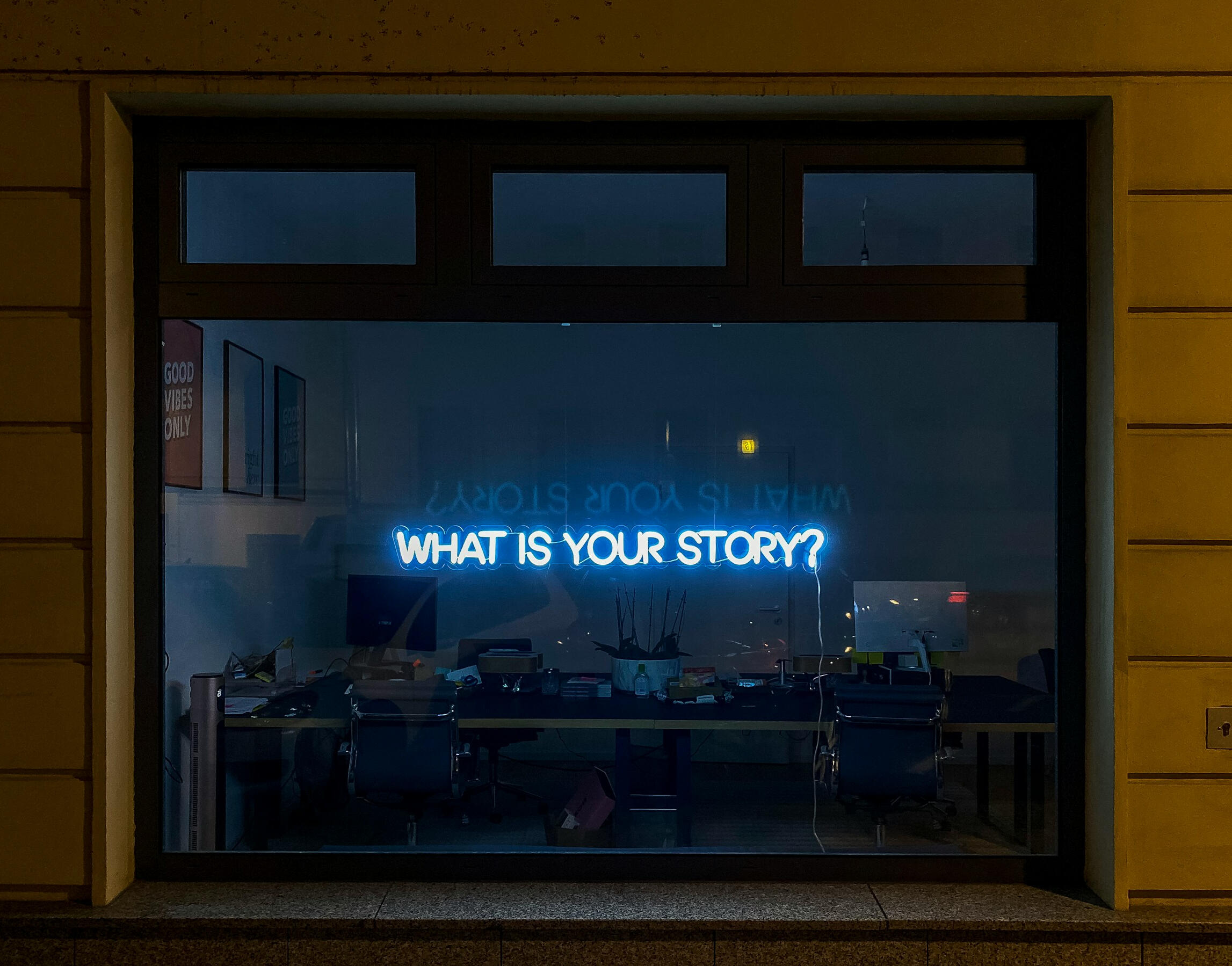the words "what is your story" is lit up on an office wall in neon
